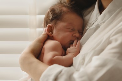 Mother holding her cute newborn baby indoors, closeup