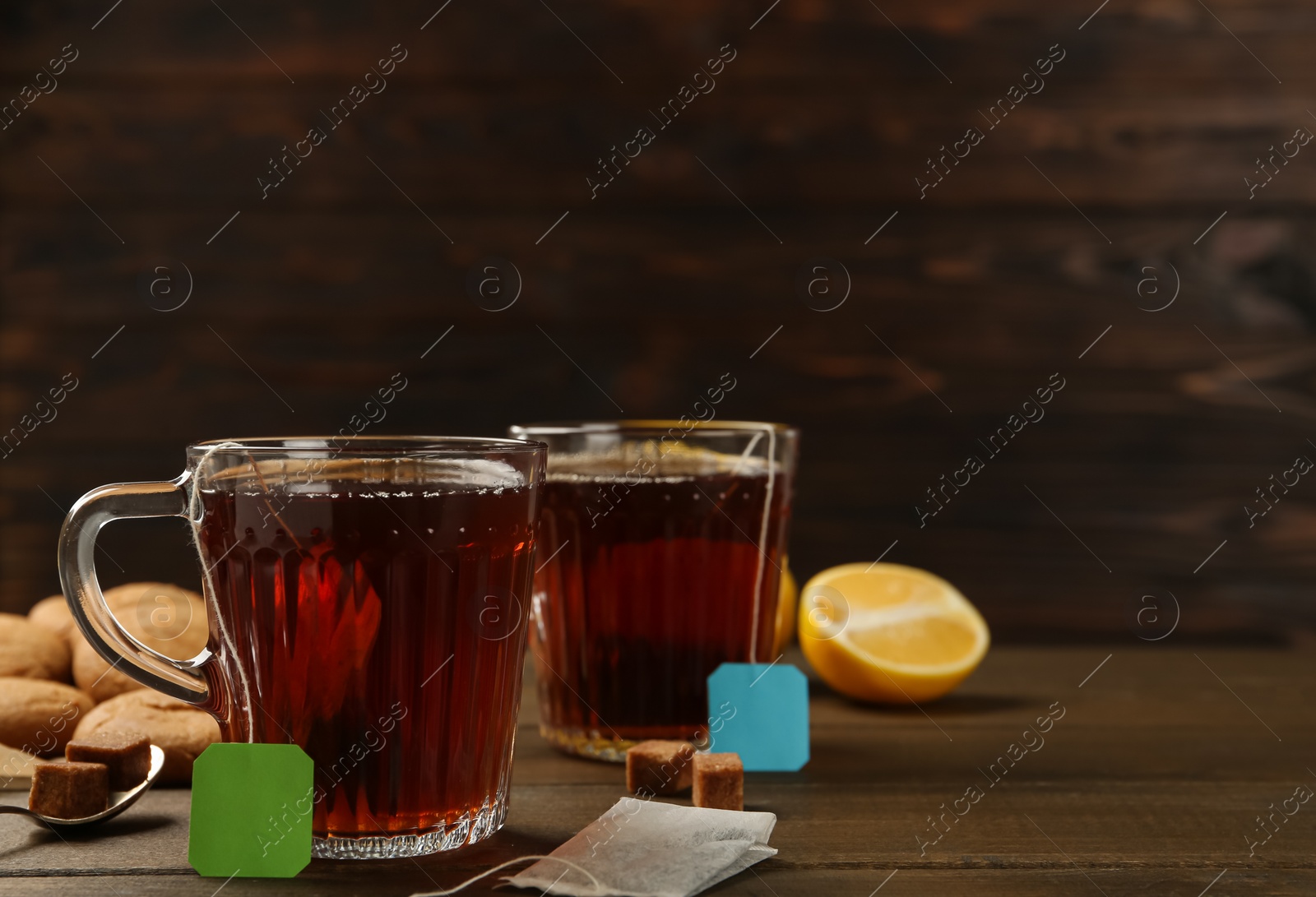 Photo of Tea bags in glass cups of hot water and sugar cubes 
on wooden table. Space for text