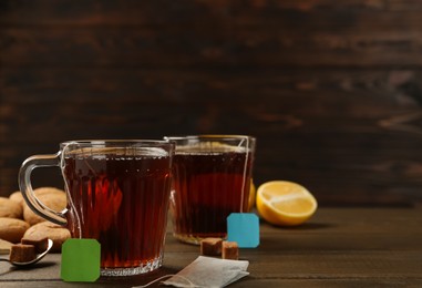 Photo of Tea bags in glass cups of hot water and sugar cubes 
on wooden table. Space for text