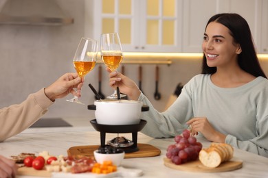 Photo of Romantic date with fondue. Couple clinking glasses of wine at home