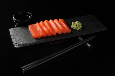 Delicious salmon sashimi, wasabi, soy sauce and chopsticks on black mirror surface