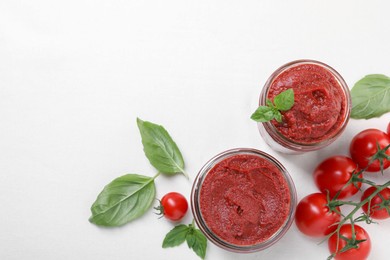 Jars of tasty tomato paste and ingredients on white table, flat lay. Space for text
