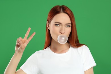 Photo of Beautiful woman blowing bubble gum and showing peace gesture on green background