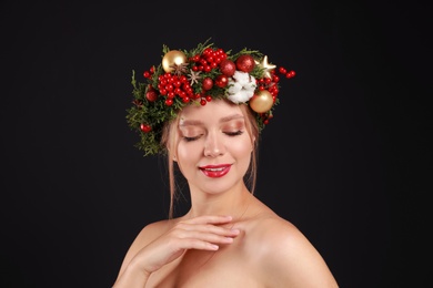 Photo of Beautiful young woman wearing Christmas wreath on black background