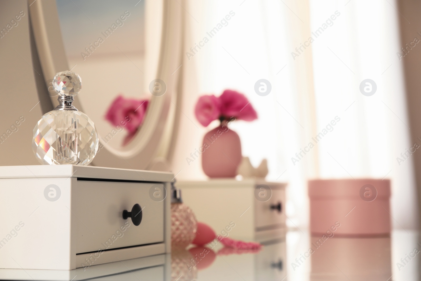 Photo of White dressing table with decor and bottles of perfumes in room