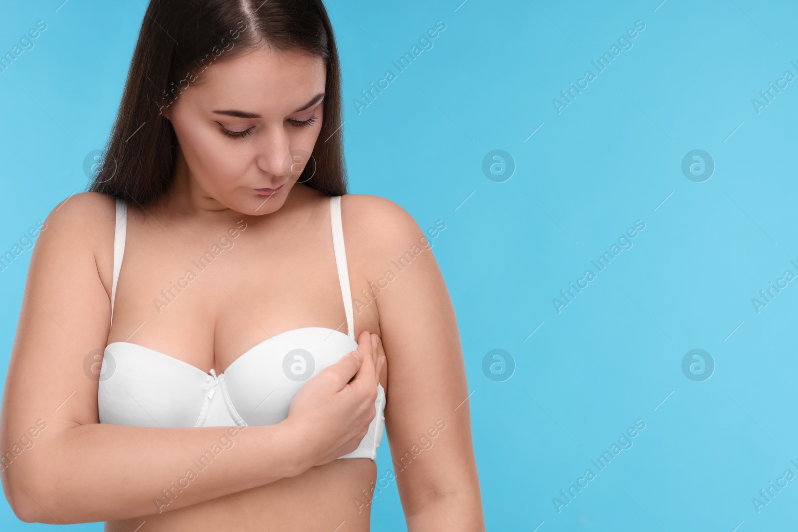 Photo of Mammology. Woman in bra doing breast self-examination on light blue background, space for text