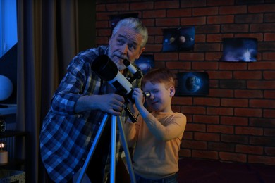 Little boy with his grandfather looking at stars through telescope in room