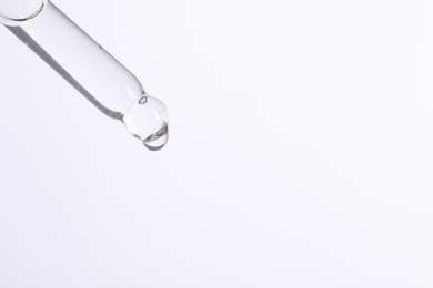 Dripping cosmetic serum from pipette on white background, space for text