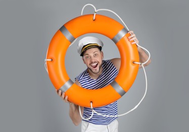 Happy sailor with orange ring buoy on grey background