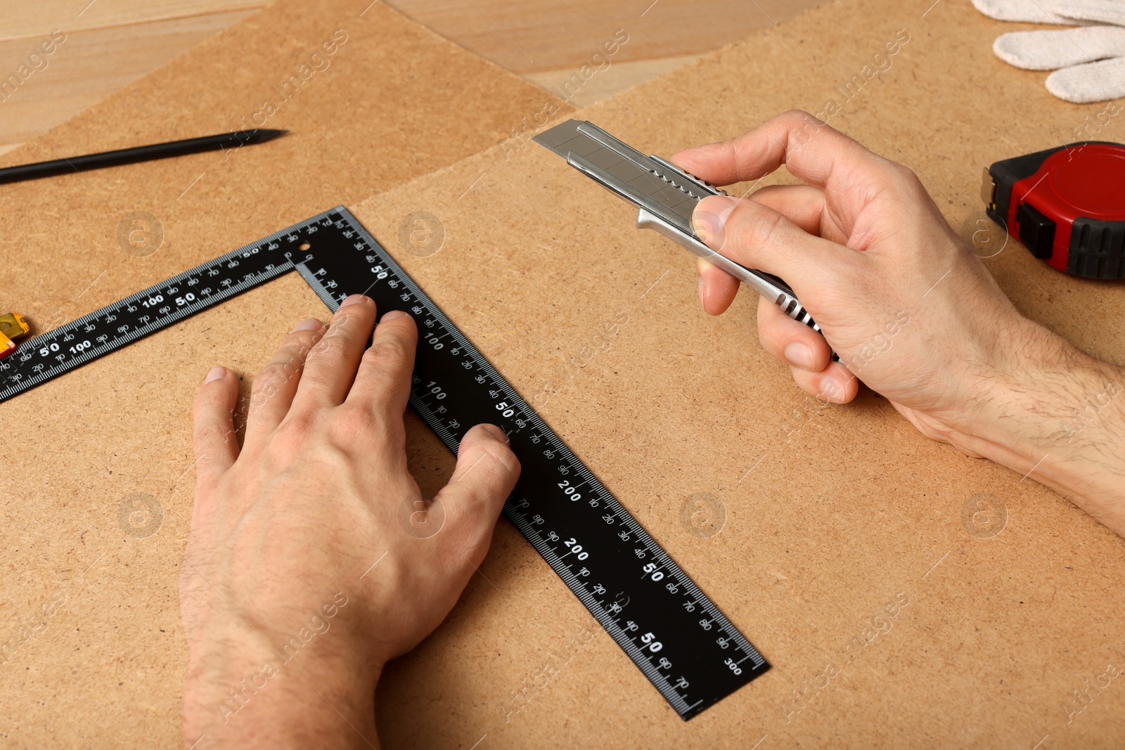 Photo of Man cutting chip board with utility knife and ruler , closeup