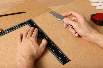 Photo of Man cutting chip board with utility knife and ruler , closeup