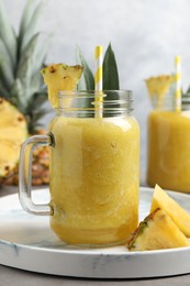 Tasty pineapple smoothie and sliced fruit on light grey table