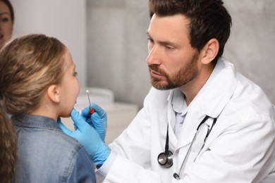 Doctor taking throat swab sample from girl`s oral cavity indoors