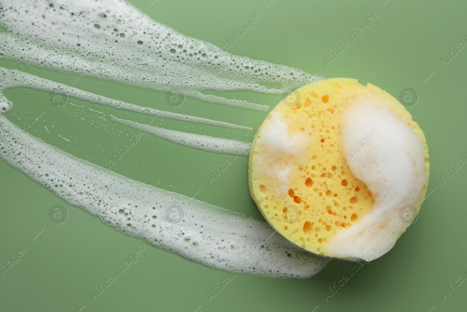 Photo of Yellow sponge with foam on green background, top view