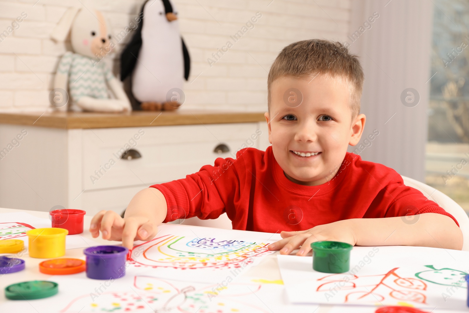 Photo of Little boy painting with finger at white table indoors