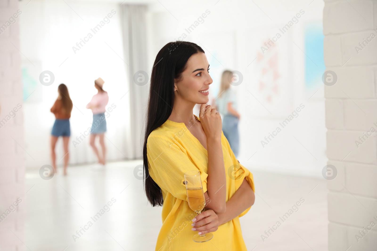 Photo of Young woman with glass of champagne at exhibition in art gallery