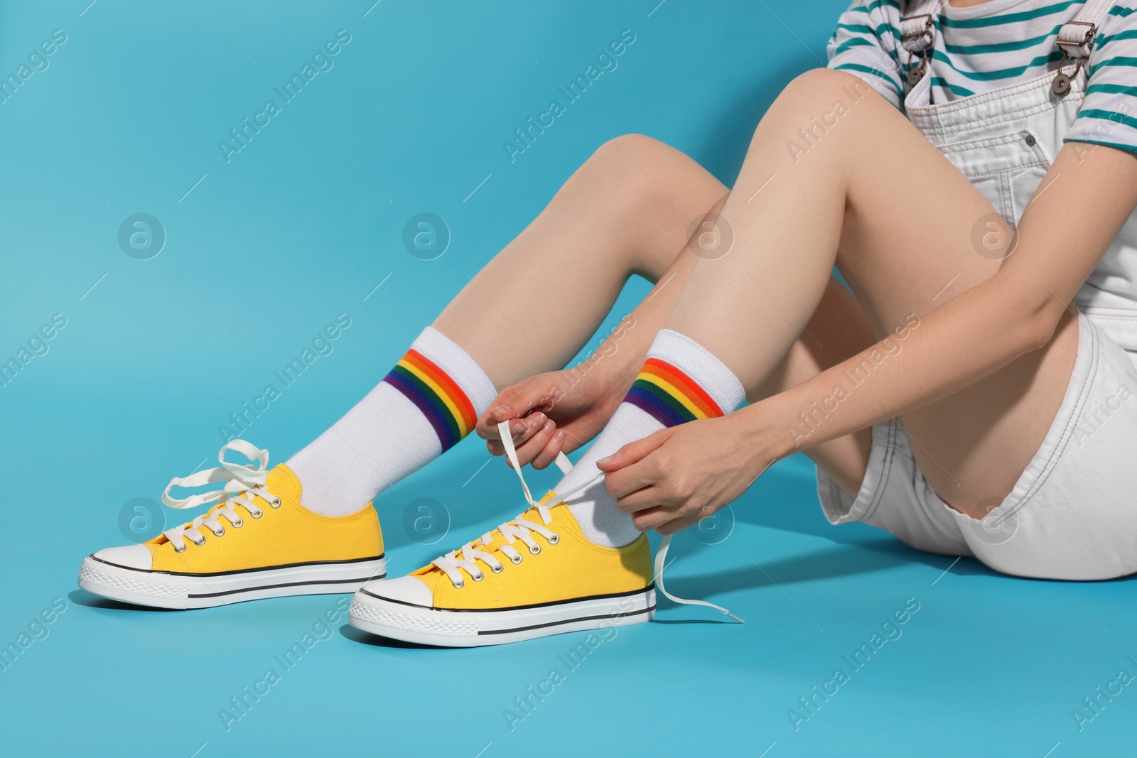 Photo of Woman lacing up yellow classic old school sneakers against light blue background, closeup