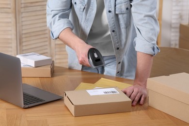 Photo of Seller with scanner reading parcel barcode at table in office, closeup. Online store