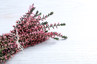 Bunch of heather branches with beautiful flowers on white wooden table, closeup. Space for text