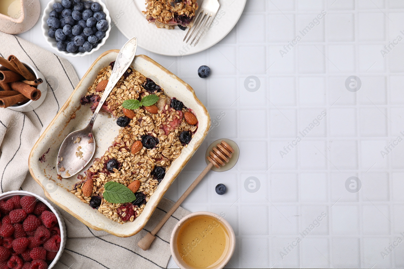 Photo of Tasty baked oatmeal with berries and almonds on white tiled table, flat lay. Space for text