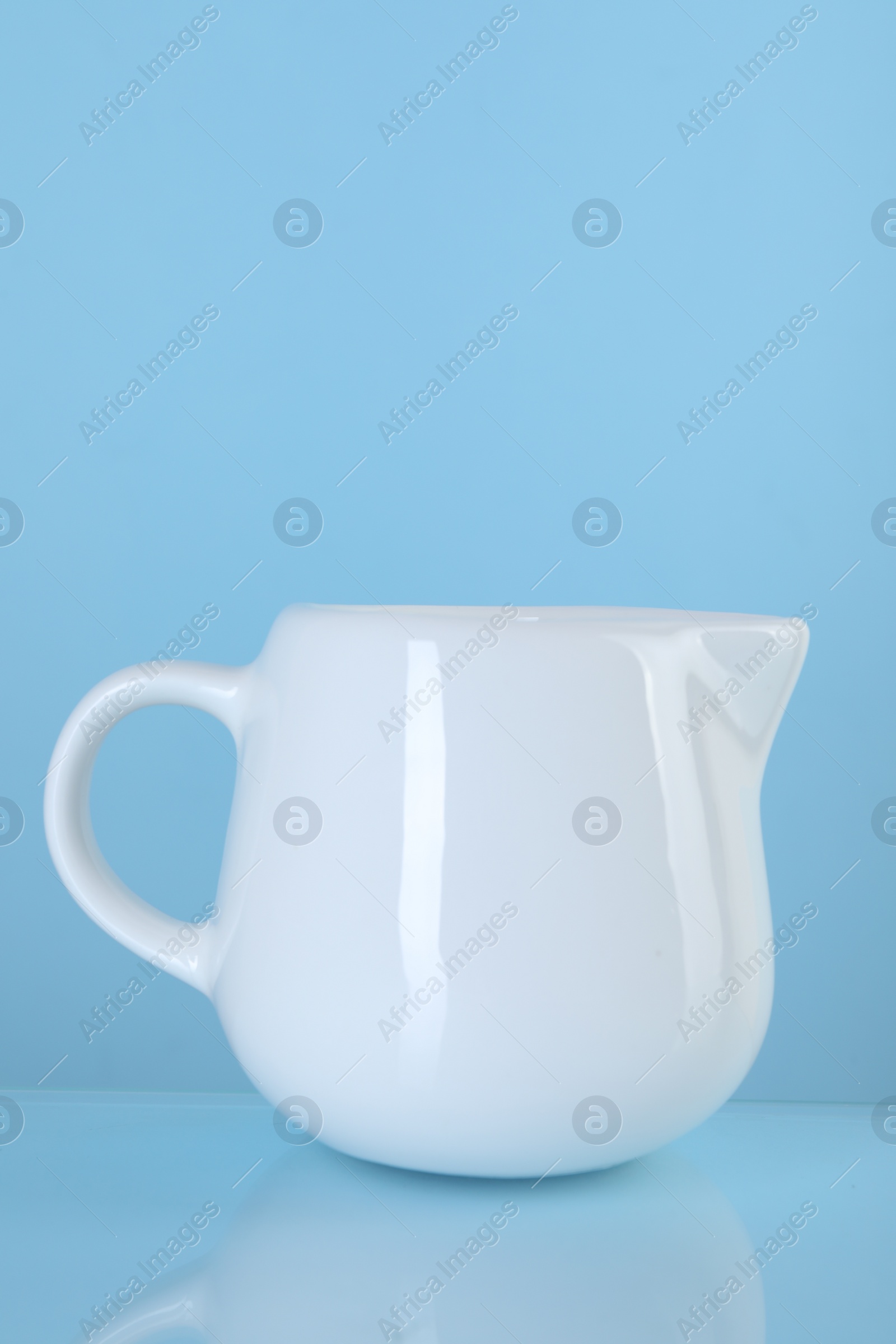 Photo of Jug of fresh milk on light blue background