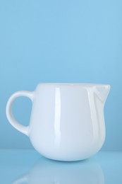 Photo of Jug of fresh milk on light blue background