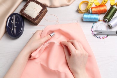 Photo of Woman with sewing needle and thread embroidering on cloth at white wooden table, top view