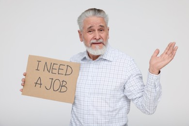 Unemployed senior man holding cardboard sign with phrase I Need A Job on white background