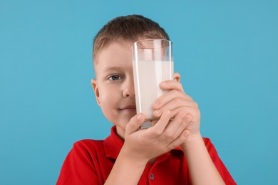 Cute boy with glass of fresh milk on light blue background