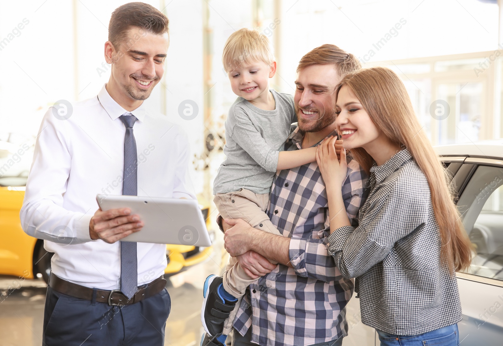 Photo of Salesman with tablet and young family in car salon