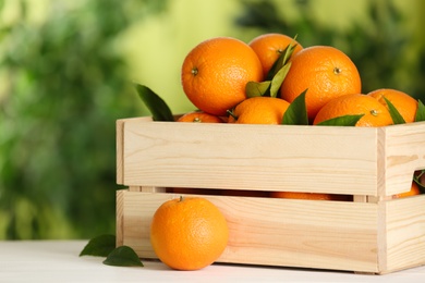 Fresh ripe oranges in wooden crate on white table against blurred background