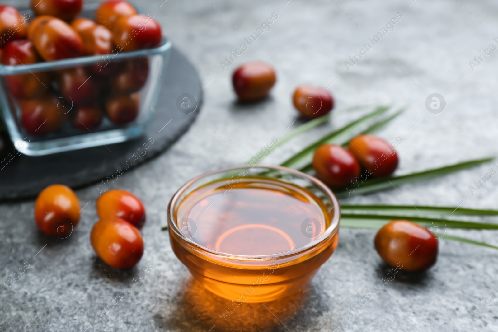 Photo of Palm oil in glass bowl, tropical leaf and fruits on grey table