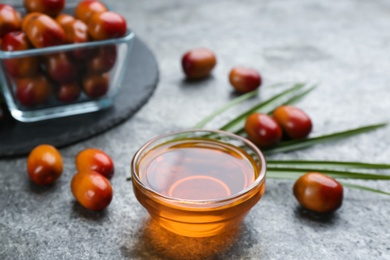 Palm oil in glass bowl, tropical leaf and fruits on grey table