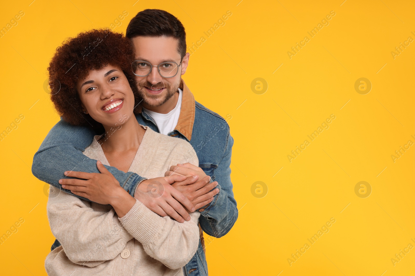 Photo of International dating. Happy couple hugging on orange background, space for text