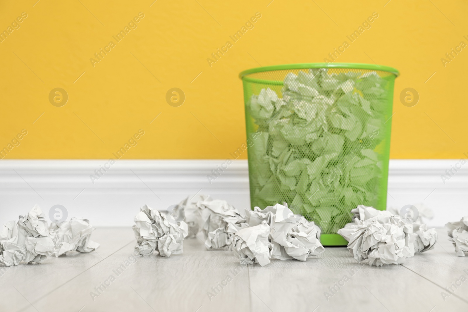 Photo of Metal bin with crumpled paper against color wall, space for text