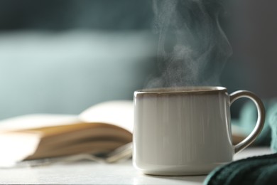 Cup of hot drink on white table against blurred background, space for text