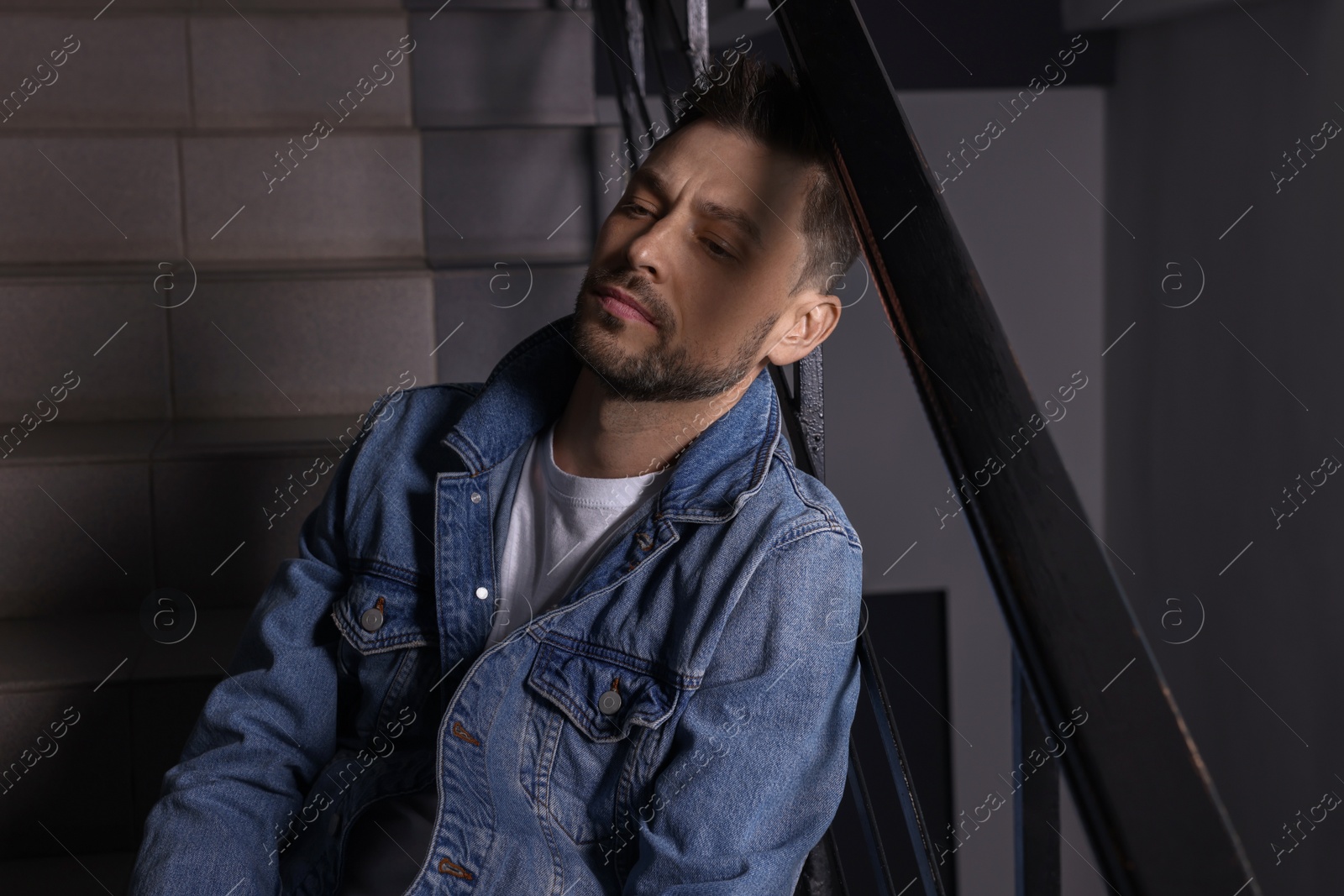 Photo of Upset man sitting on stairs indoors. Loneliness concept