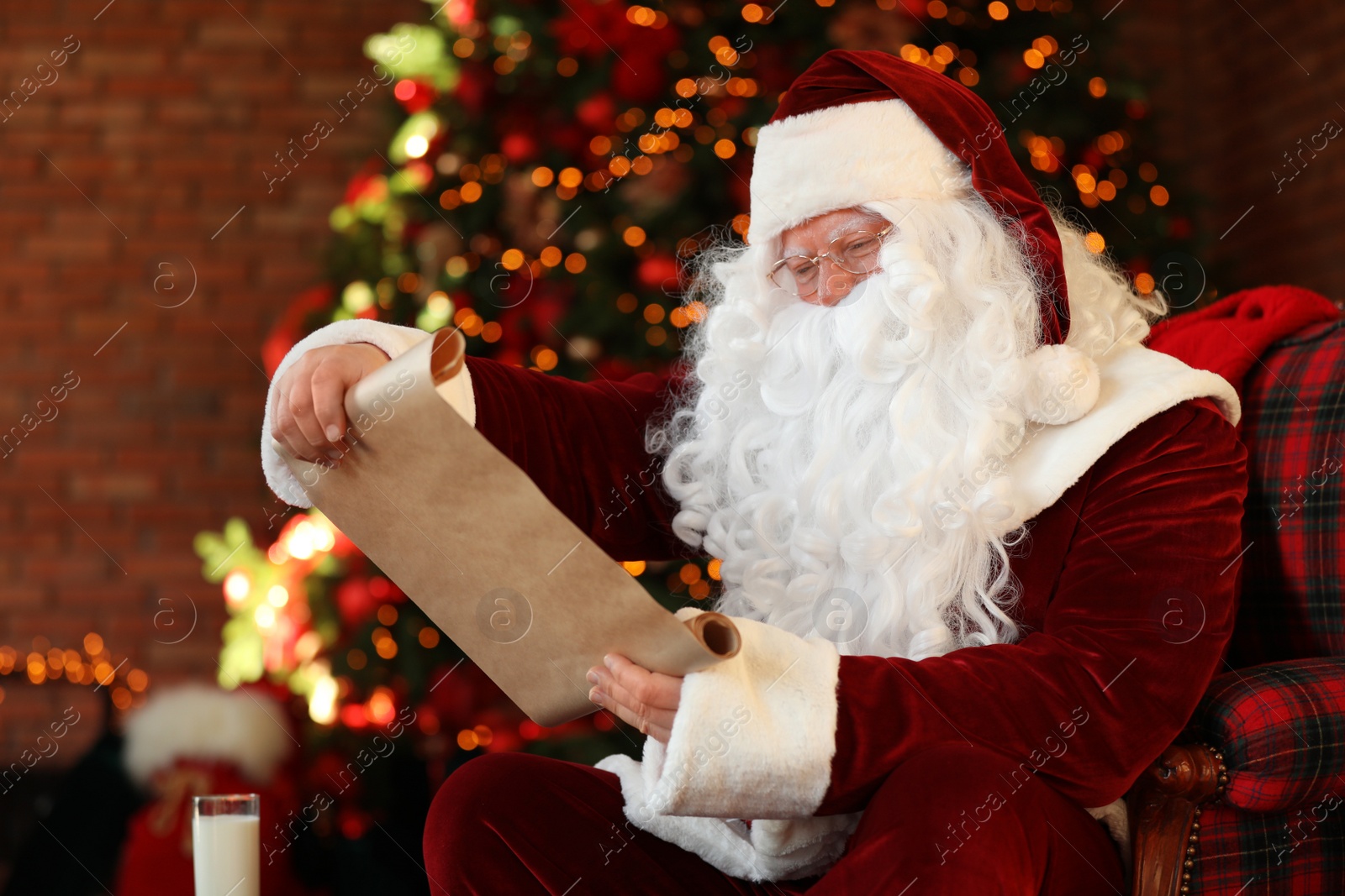 Photo of Santa Claus with wish list near Christmas tree indoors