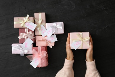 Woman with gift box at black table, top view. Advent calendar