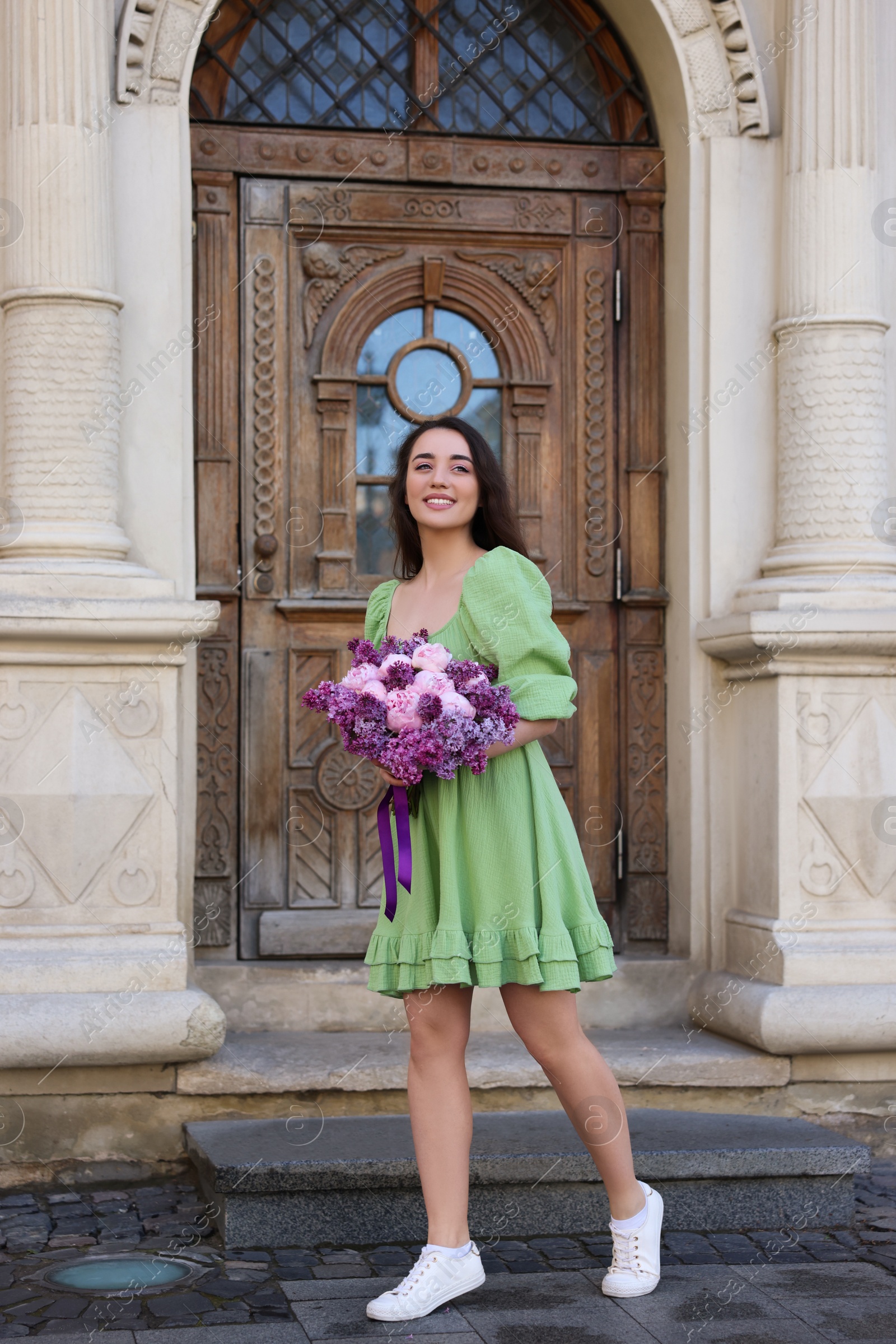 Photo of Beautiful woman with bouquet of spring flowers near building outdoors