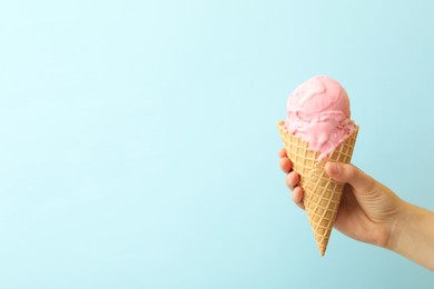 Woman holding waffle cone with delicious pink ice cream on light blue background, closeup. Space for text