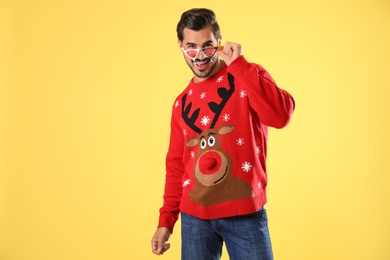 Photo of Happy man in Christmas sweater and party glasses on yellow background