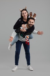 Photo of Happy young couple in Christmas sweaters and reindeer headbands on grey background