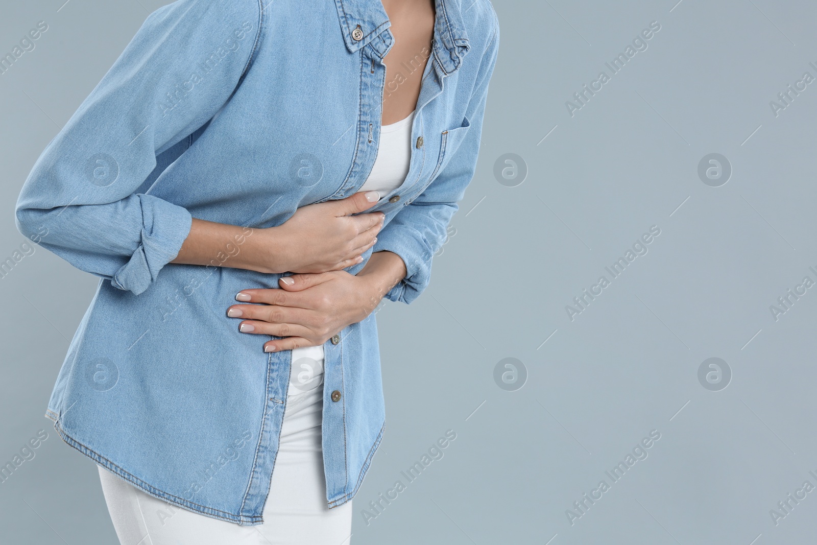 Photo of Closeup view of woman suffering from stomach ache on grey background, space for text. Food poisoning