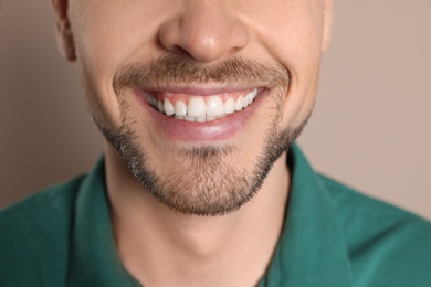 Smiling man with perfect teeth on color background, closeup