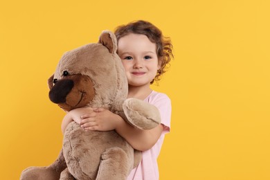 Photo of Cute little girl with teddy bear on orange background