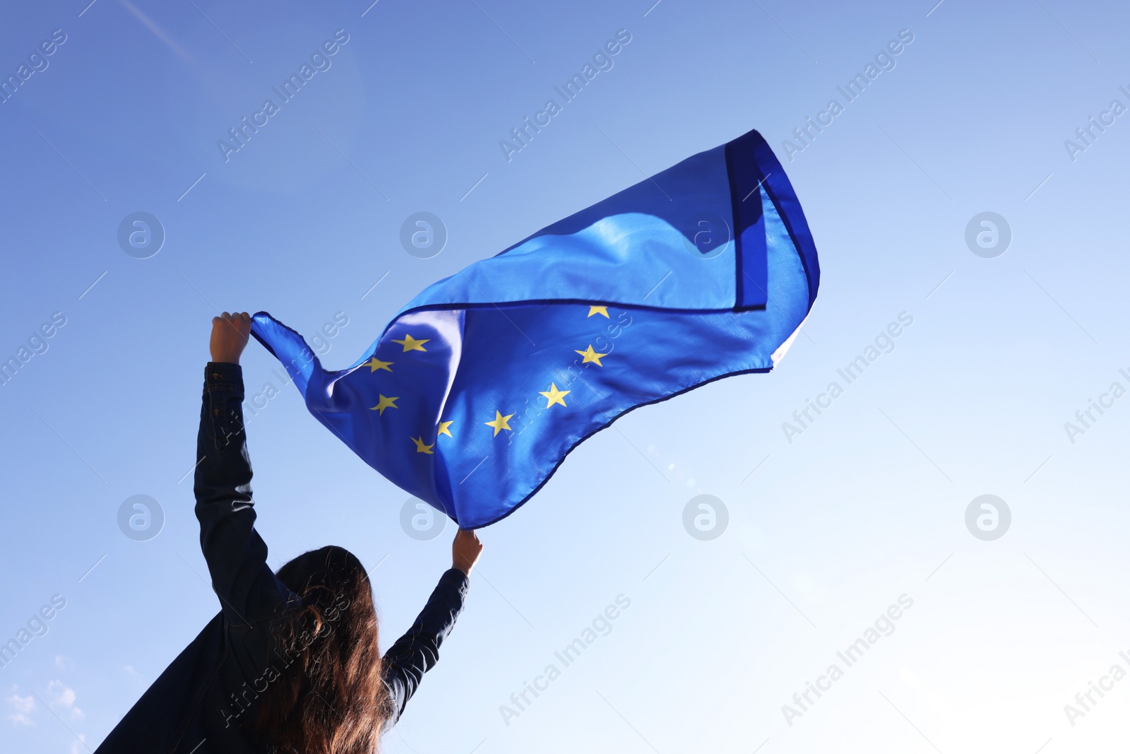 Photo of Woman holding European Union flag against blue sky outdoors, low angle view