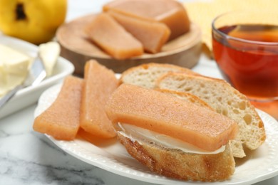 Photo of Delicious quince paste and bread on white marble table, closeup