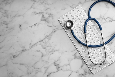 Photo of Keyboard and stethoscope on white marble table, flat lay with space for text. Concept of technical support