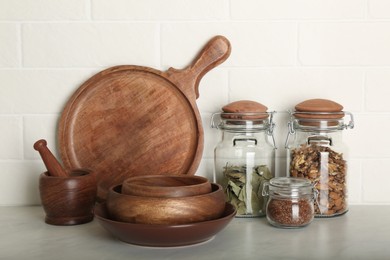 Photo of Wooden dishware and different products on grey table near white brick wall in kitchen